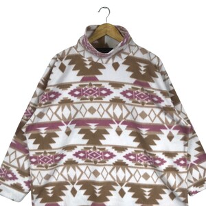 Puede incluir: Sudadera de vell&oacute;n blanca con un patr&oacute;n geom&eacute;trico marr&oacute;n y rosa. La sudadera tiene cuello alto y mangas largas.