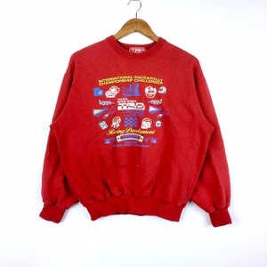 May include: Red sweatshirt with a colourful graphic print featuring the text "International Race & Rally Championship Challenger", "Toyota Motor Sports", "TRD", and "Racing Development".