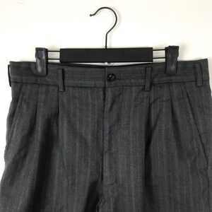 May include: Grey pinstripe dress trousers with a button fastening and pleats. The trousers are hanging on a black hanger.