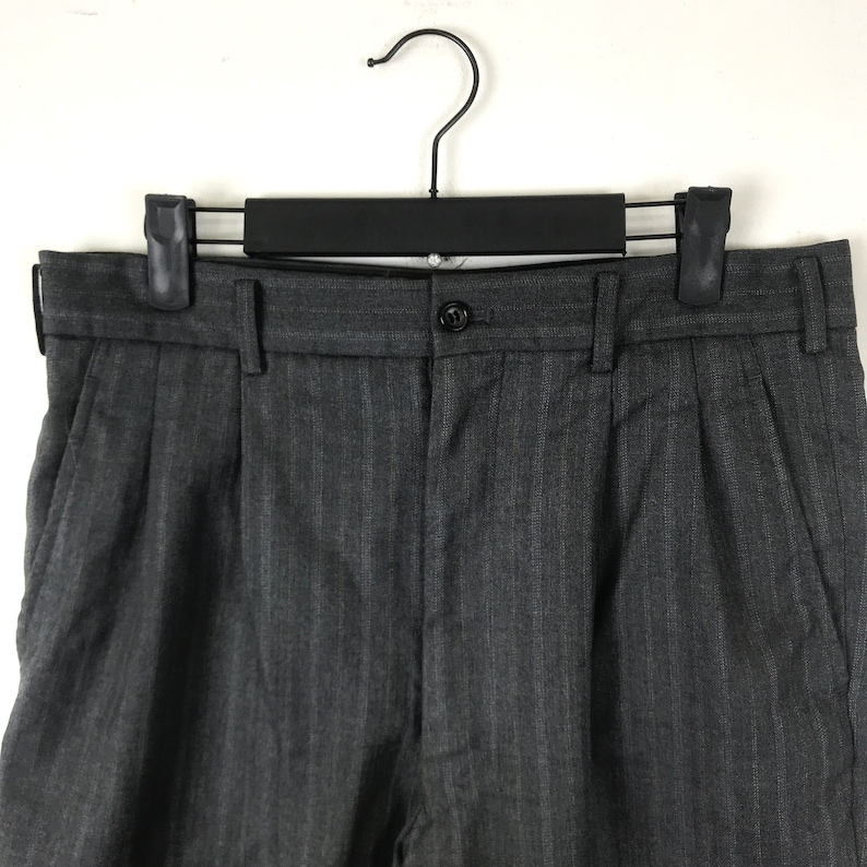 May include: Grey pinstripe dress trousers with a button fastening and pleats. The trousers are hanging on a black hanger.