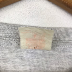 May include: A close-up of a white tag with a faded orange label attached to a gray shirt.