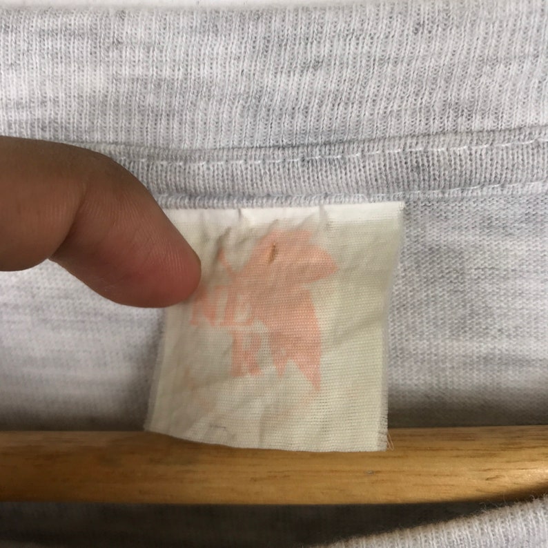 May include: A close-up of a white tag with a pink stain. The tag is attached to a gray t-shirt.