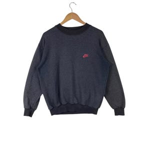 May include: A dark grey sweatshirt with a red Nike logo on the left chest.