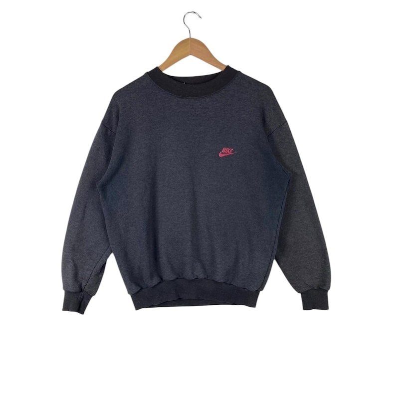 May include: A dark grey sweatshirt with a red Nike logo on the left chest.