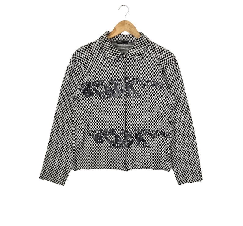 Puede incluir: Chaqueta a cuadros en blanco y negro con cierre de cremallera y el texto "Comme des Gar&ccedil;ons" impreso en la parte delantera.