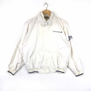 May include: White zippered jacket with blue trim and the logo "Le Coq Sportif" on the front.