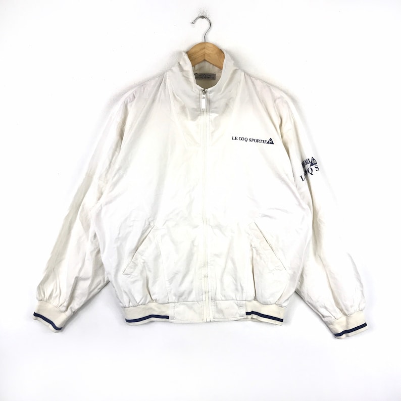 May include: White zippered jacket with blue trim and the logo "Le Coq Sportif" on the front.