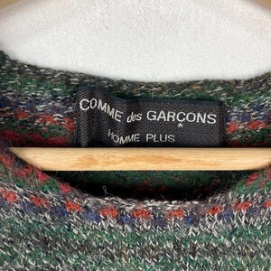 May include: A green, red, and blue patterned sweater with a black label that reads "COMME des GAR&Ccedil;ONS HOMME PLUS".