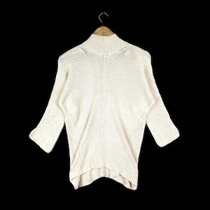 May include: A cream-colored knitted sweater with a mock neck and 3/4 sleeves. The sweater has a relaxed fit and a slightly longer length in the back.
