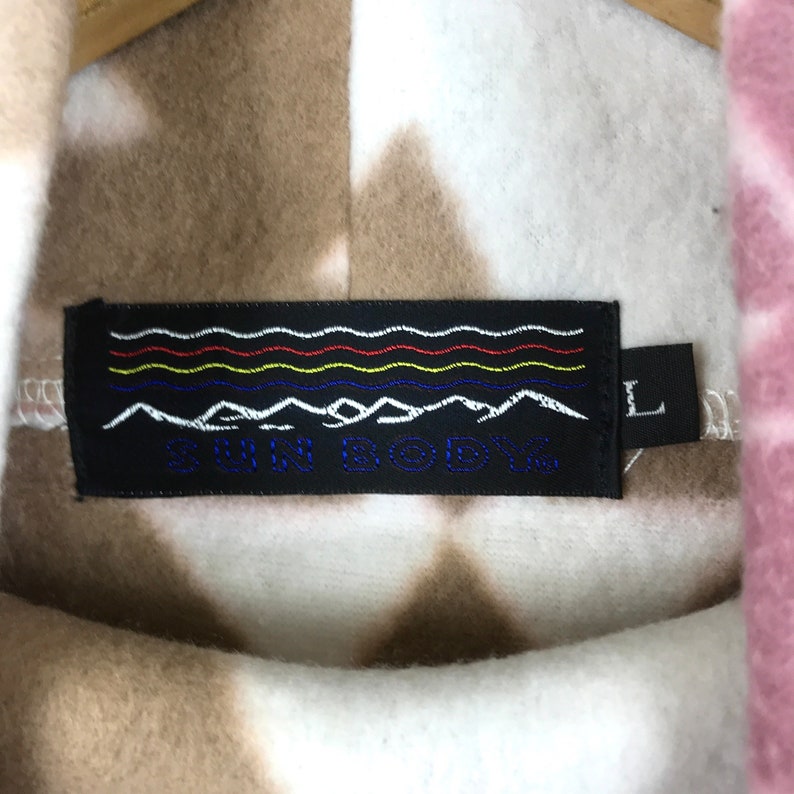 Puede incluir: Una sudadera con capucha de polar tie-dye blanca, marr&oacute;n y rosa con una etiqueta negra que dice "SUN BODY" y una etiqueta de talla "L".