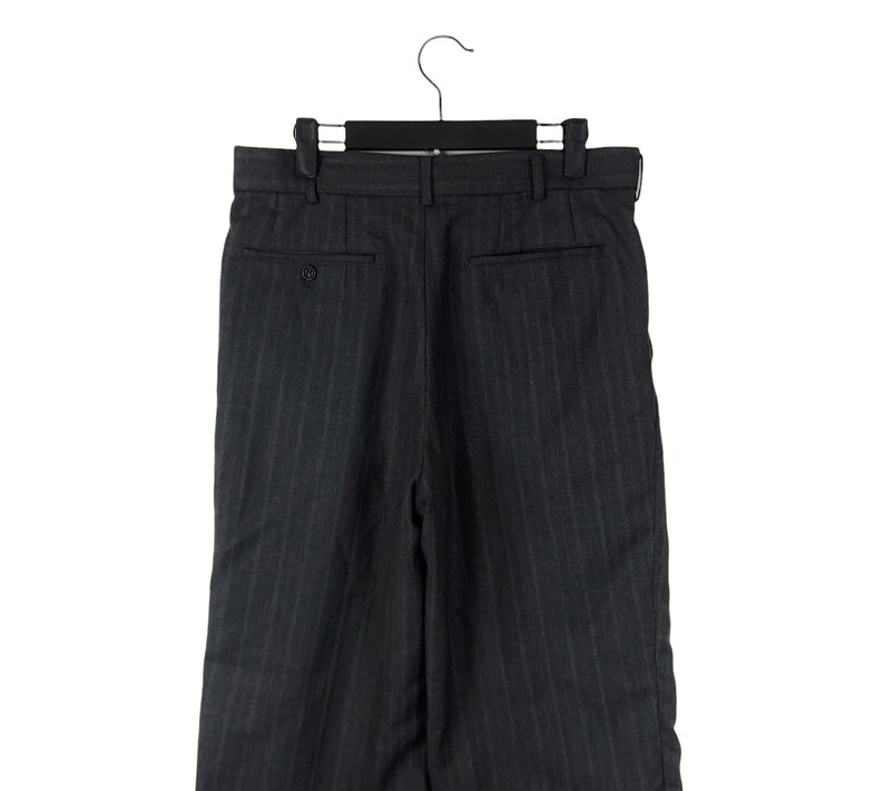 May include: Dark grey pinstripe trousers with a button fly and a back pocket. The trousers are hanging on a black hanger.