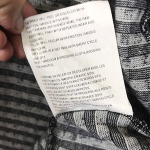 Puede incluir: Una etiqueta blanca con texto negro que detalla las instrucciones de cuidado para una prenda. La impresi&oacute;n se pelar&aacute; o decolorar&aacute; con la fricci&oacute;n, manip&uacute;lela con cuidado. Este art&iacute;culo tiene dobladillos sin terminar, los bordes sin procesar se deshilachar&aacute;n con el uso y la limpieza repetidos. La formaci&oacute;n de bolitas ocurrir&aacute; con la fricci&oacute;n, manip&uacute;lela con cuidado. Limpieza en seco en una bolsa de red con ciclo corto. Secar en l&iacute;nea. Planchar a trav&eacute;s de un pa&ntilde;o de planchado, evitando la impresi&oacute;n.