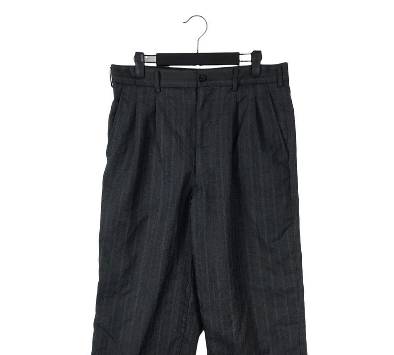 May include: A pair of dark grey pinstripe trousers with a pleat in the front. The trousers are hanging on a black hanger.