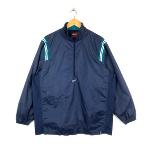 May include: A navy blue windbreaker jacket with a half-zip closure, white and teal stripes on the sleeves, and a white Nike swoosh logo on the chest.