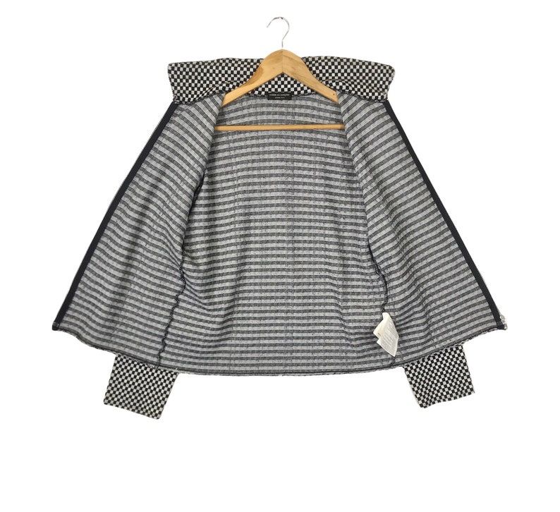 Puede incluir: Chaqueta a rayas blancas y negras con un patr&oacute;n a cuadros en el cuello y los pu&ntilde;os. La chaqueta est&aacute; abierta y el forro es visible.