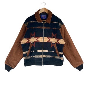 May include: A vintage zip-up jacket with a brown corduroy collar and sleeves. The body of the jacket is black with a geometric pattern in tan and brown. The jacket is hanging on a wooden hanger.