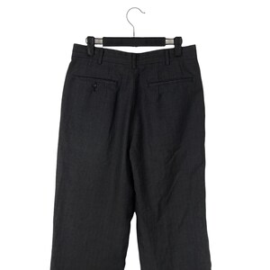 May include: Dark gray dress pants with a subtle pinstripe pattern, hanging on a black hanger. The pants have a buttoned back pocket and a classic tailored design, suitable for formal or business attire.