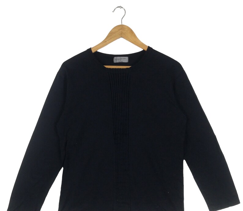 May include: A black long-sleeved shirt with a vertical seam down the front. The shirt has a round neckline.