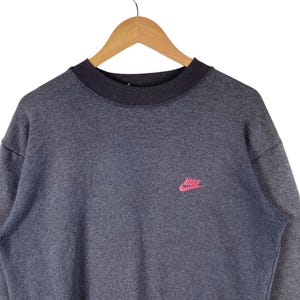 May include: A grey sweatshirt with a pink Nike logo on the front.