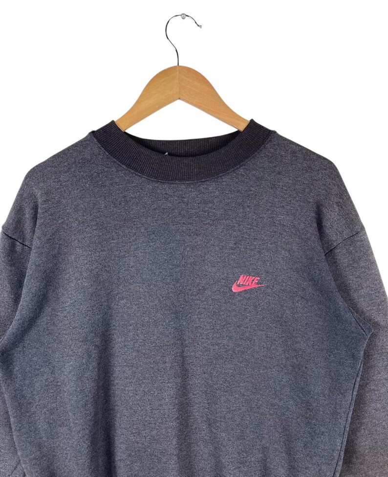 May include: A grey sweatshirt with a pink Nike logo on the front.