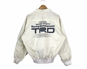 May include: A white jacket with a black and blue logo that says "Toyota Motor Sports Racing Development TRD".