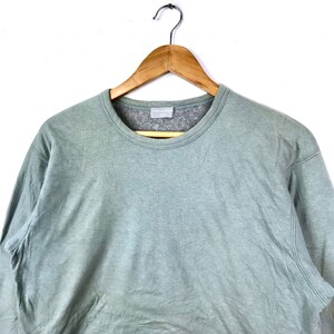 Op de afbeelding: Een lichtgroen longsleeve sweatshirt met een ronde hals. Het sweatshirt hangt aan een houten hanger.