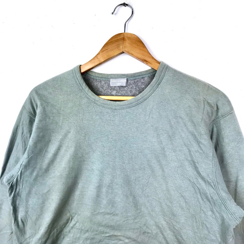 Op de afbeelding: Een lichtgroen longsleeve sweatshirt met een ronde hals. Het sweatshirt hangt aan een houten hanger.