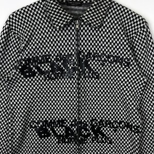 Puede incluir: Camisa de manga larga a cuadros en blanco y negro con el texto "Comme des Gar&ccedil;ons" repetido en un estampado gr&aacute;fico negro.