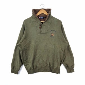 May include: A green fleece sweatshirt with a brown collar and a button closure. The sweatshirt has an embroidered logo that says "Ralph Lauren, Chaps 1978" and features a deer with antlers.