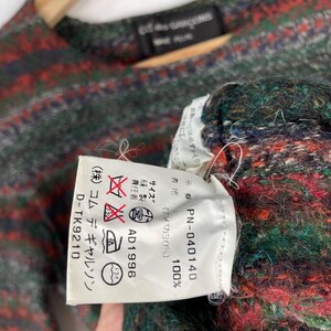May include: A white tag with black text detailing the care instructions for a garment. The tag reads "(株) コムデギャルソン D-TK9210", "ドライ", "AD1996", "品番 PN-040140", "表地 100% (アルパカ30%)", and "おかには必ずェイク)".
