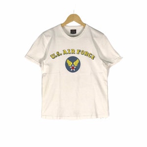 May include: White t-shirt with a blue and yellow U.S. Air Force logo. The logo features a red star and wings.