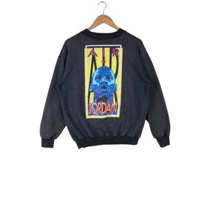 May include: A dark grey sweatshirt with a large graphic print on the back. The graphic features a yellow rectangle with the text "AIR BY JORDAN" in red, black, and white. Inside the rectangle is a blue and white image of Michael Jordan.