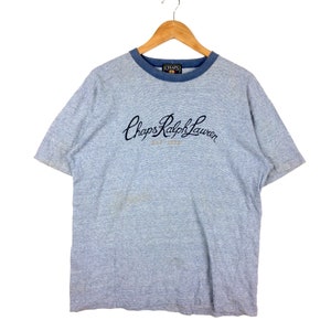Peut inclure: Un t-shirt gris à manches courtes avec une bordure bleue autour du cou. Le t-shirt a un logo brodé bleu marine qui dit "Chaps Ralph Lauren Est. 1978".
