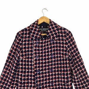 May include: A double-breasted navy blue jacket with a geometric pattern in white and red. The jacket is hanging on a wooden hanger. The label reads "JUNYA WATANABE COMME des GAR&Ccedil;ONS".