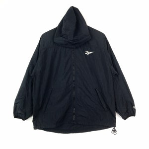 Op de afbeelding: Een zwarte capuchontrui met een rits en een wit Reebok-logo op de borst.
