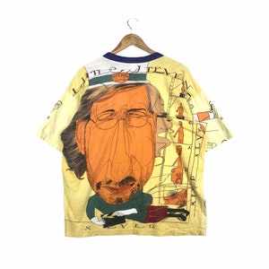 May include: Yellow short-sleeved t-shirt with a cartoon illustration of a man wearing a captain's hat and glasses. The text "Little J.  Teve" is printed on the shirt.