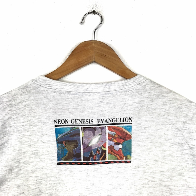 May include: A heather grey t-shirt with a graphic print of three robots from the anime series Neon Genesis Evangelion. The text "NEON GENESIS EVANGELION" is printed above the robots.