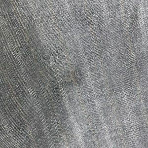 May include: Close-up of a dark grey denim fabric with a subtle herringbone weave. The fabric has a slightly textured surface and a faded appearance.