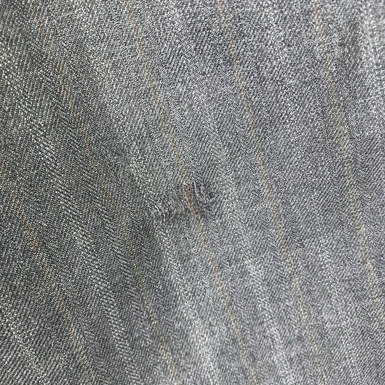 May include: Close-up of a dark grey denim fabric with a subtle herringbone weave. The fabric has a slightly textured surface and a faded appearance.