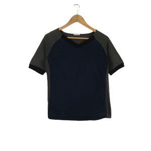 May include: A short-sleeved, V-neck t-shirt with a two-tone design. The shirt is grey with a navy blue panel in the front. The shirt has a small red label with the word "MARNI" on it.