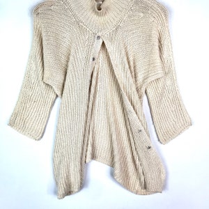 May include: A cream-colored knitted cardigan with a button closure and a slightly asymmetrical hem.