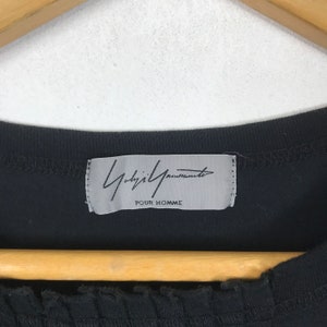 May include: A black t-shirt with a white label that says "Yohji Yamamoto POUR HOMME".