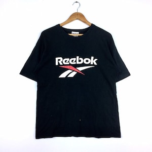 Op de afbeelding: Zwart T-shirt met een wit Reebok-logo en een rode accent. Het logo bevat de naam Reebok en een gestileerde vectorafbeelding.