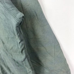 Op de afbeelding: Close-up van een groene stof met een gladde textuur. De stof is over zichzelf gevouwen, waardoor een vouw ontstaat.