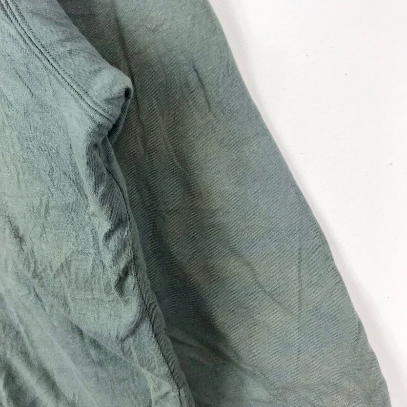 Op de afbeelding: Close-up van een groene stof met een gladde textuur. De stof is over zichzelf gevouwen, waardoor een vouw ontstaat.