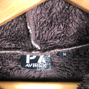 May include: A brown fleece jacket with a black patch that says "PX AVIR" and a size tag that says "M".