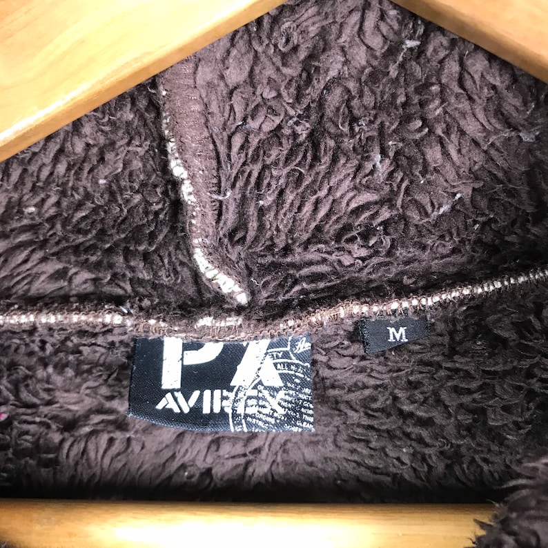 May include: A brown fleece jacket with a black patch that says "PX AVIR" and a size tag that says "M".