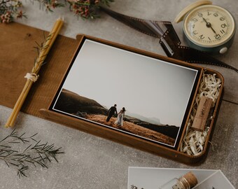 Op de afbeelding: Een houten doos met een scharnierend deksel, met daarin een foto van een stel dat op een heuveltop loopt, een USB-stick met de tekst "Light & Stone" erop gegraveerd en een klein beetje gescheurd papier.