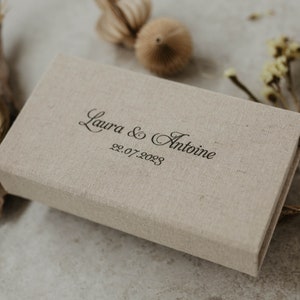 May include: A beige linen box with the text "Laura & Antoine 22.07.2023" printed on the top.