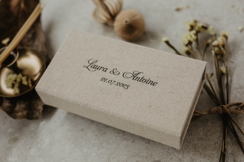 May include: A beige linen box with the text "Laura & Antoine 22.07.2023" printed on the top.